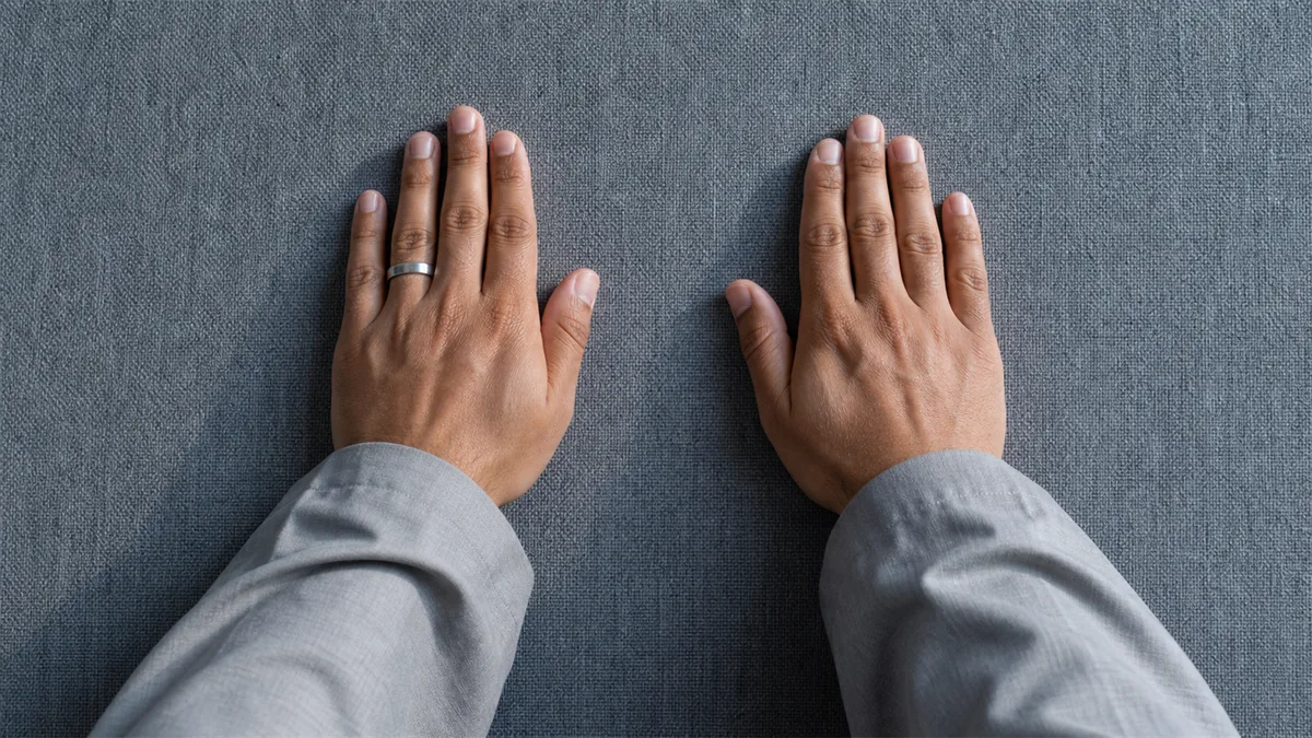Hands placed flat for sujud on a plain prayer mat, with a steel smart ring left untouched
