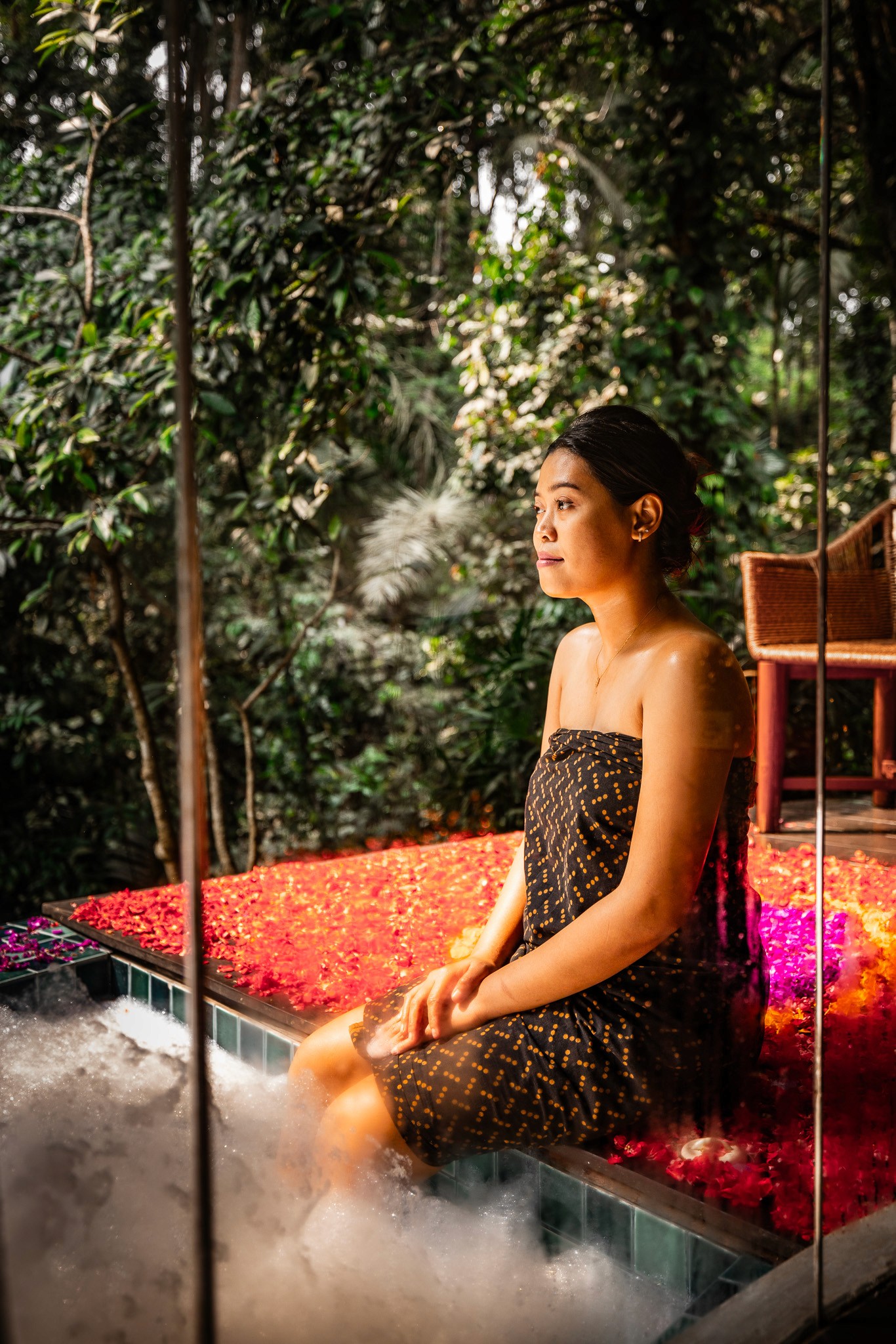 Eine Frau entspannt sich an einem mit Blüten bedeckten Jacuzzi im luxuriösen Spa-Bereich des Ning Resort Ubud