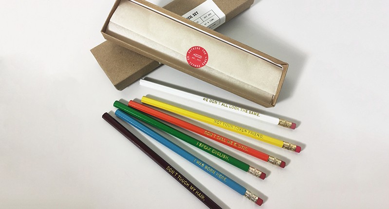 A photo of an opened box and some black, blue, green, red, yellow and white crayons near it.