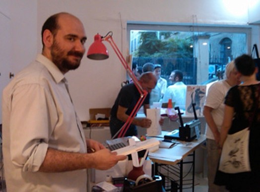 A picture of a man holding a book while sitting in a paper printing making shop.