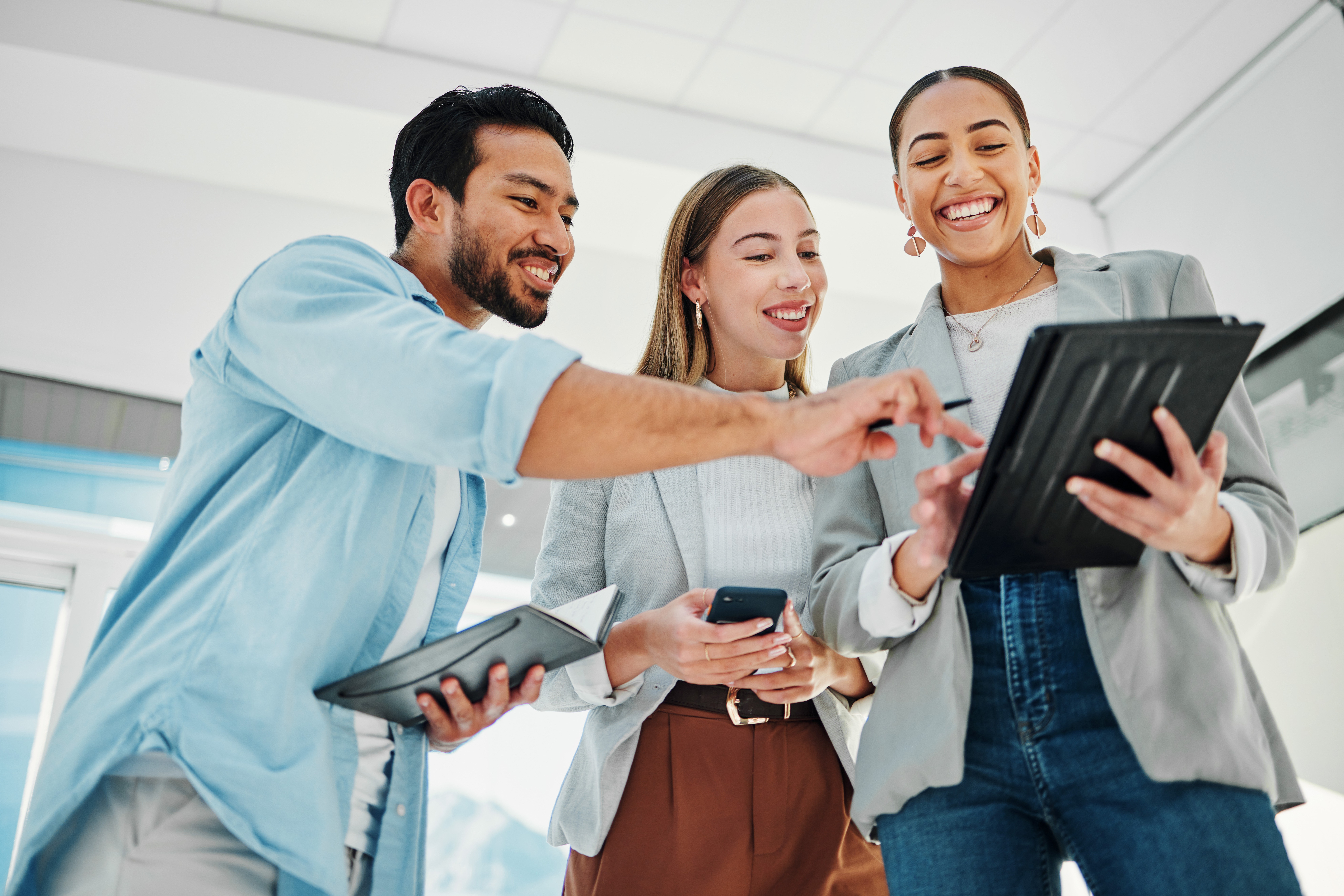 Three coworkers smiling while looking at a tablet together in an office