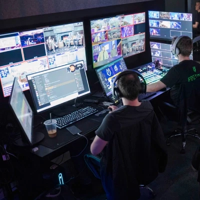 Two broadcast staff are sitting at their desks monitoring a live production