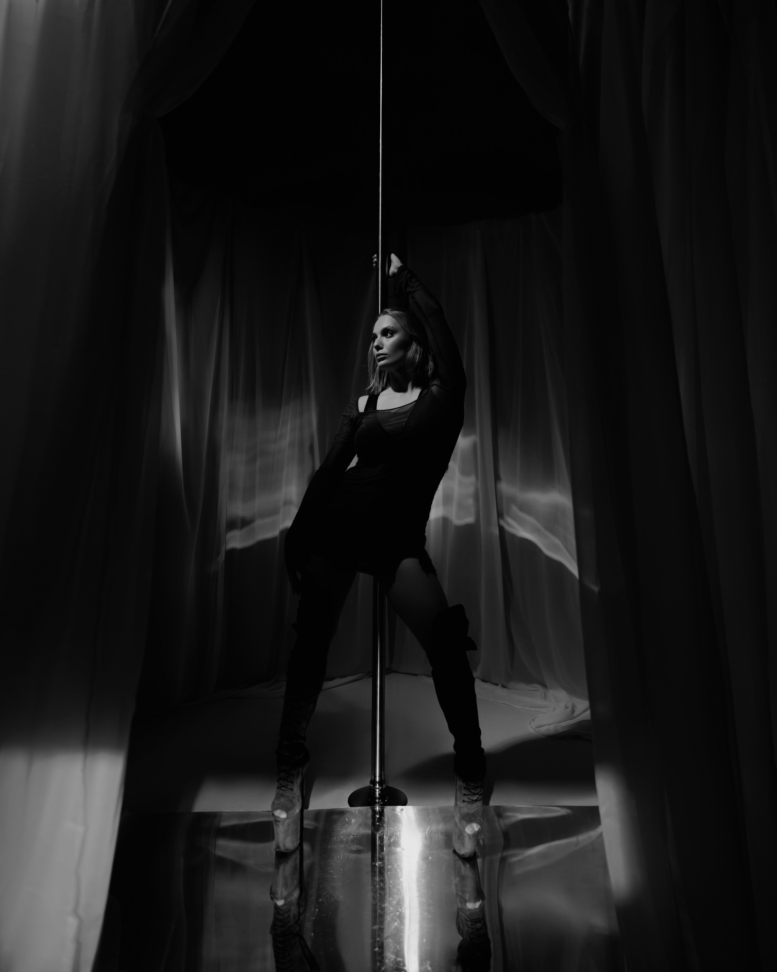 A confident person with short, styled hair and a leather jacket poses against a dark backdrop.