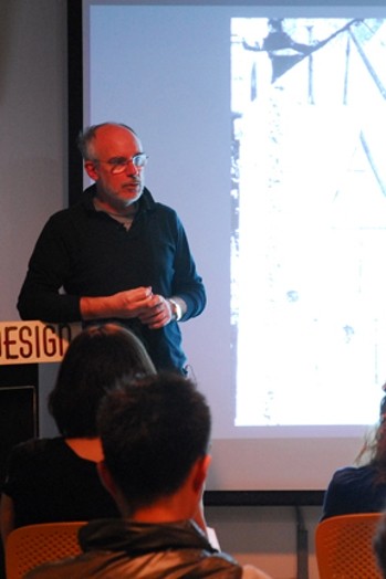 A man giving a lecture while having behind him a screen projection.