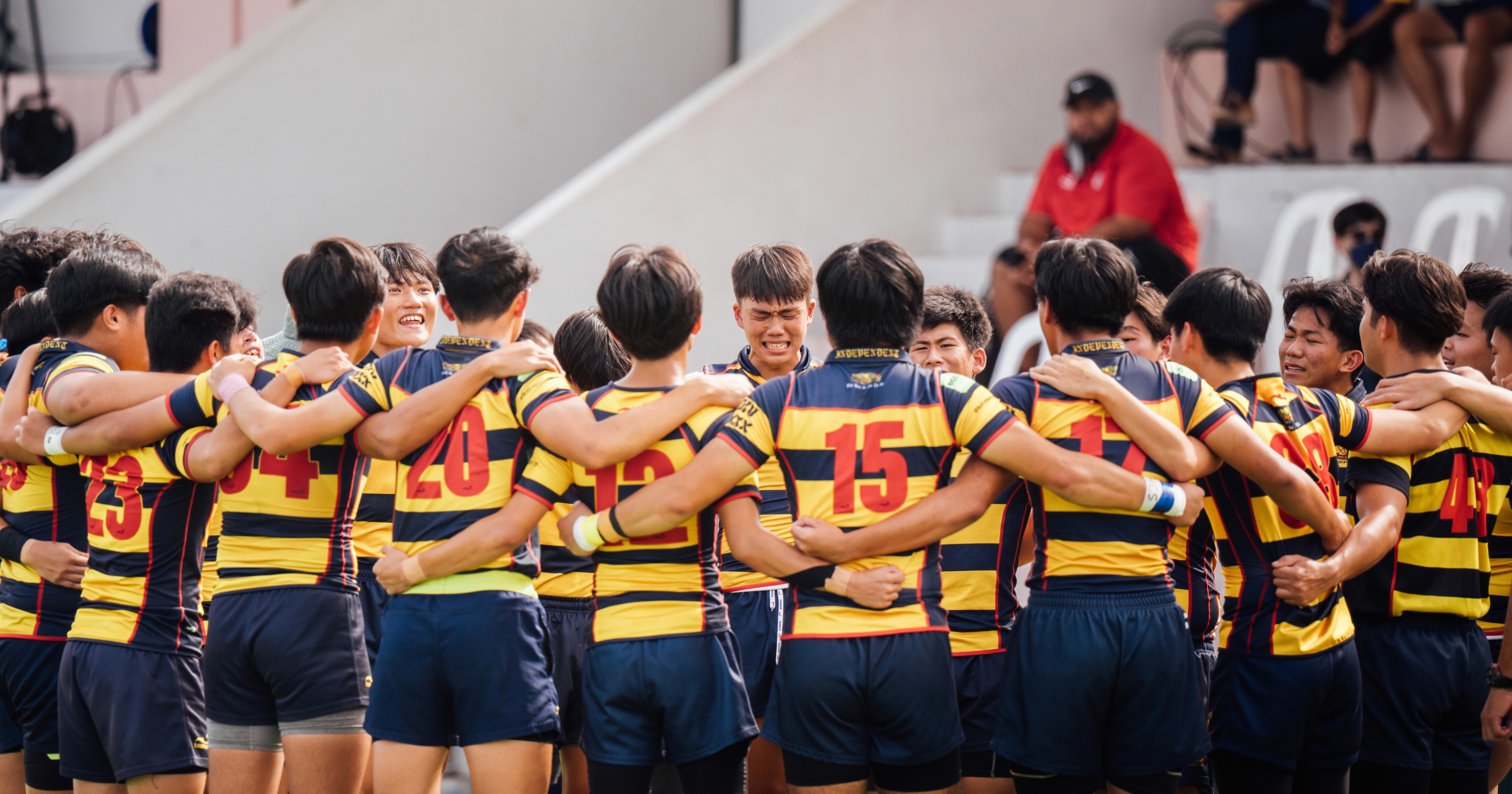 The ACS (yellow stripes) rugby team members huddling together on the field during the A Division final at MOE Evans Road field.