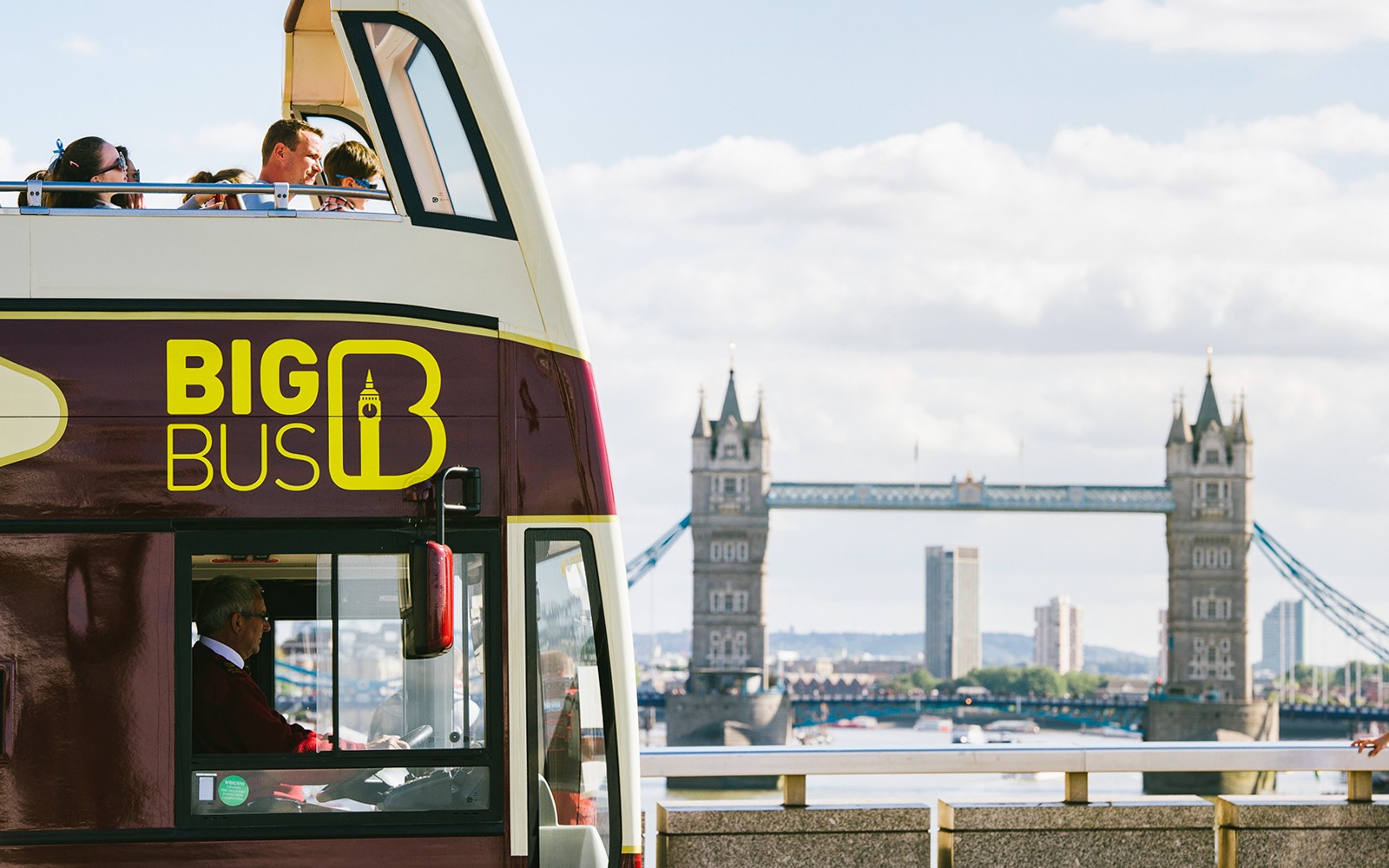 Big Bus tour passing near London Tower Bridge with view of Thames River.