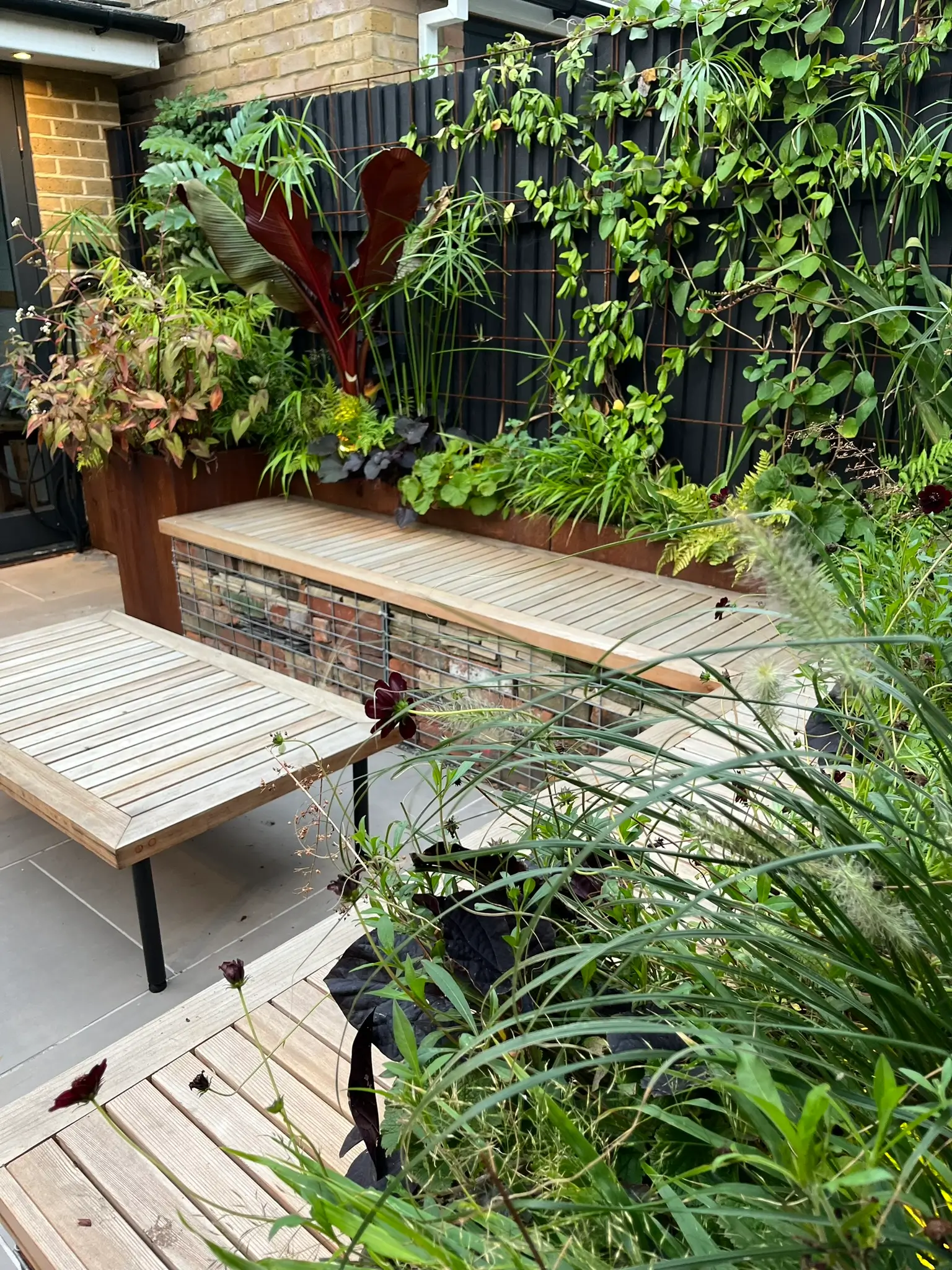 A cozy outdoor space with wooden tables surrounded by lush greenery and potted plants.