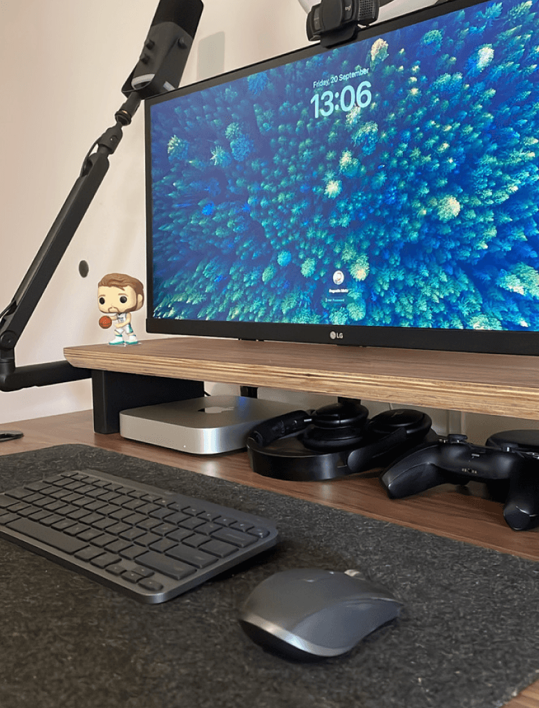 Setup de computador organizado, com monitor grande exibindo um fundo azul, teclado, mouse e acessórios sobre uma mesa de madeira.