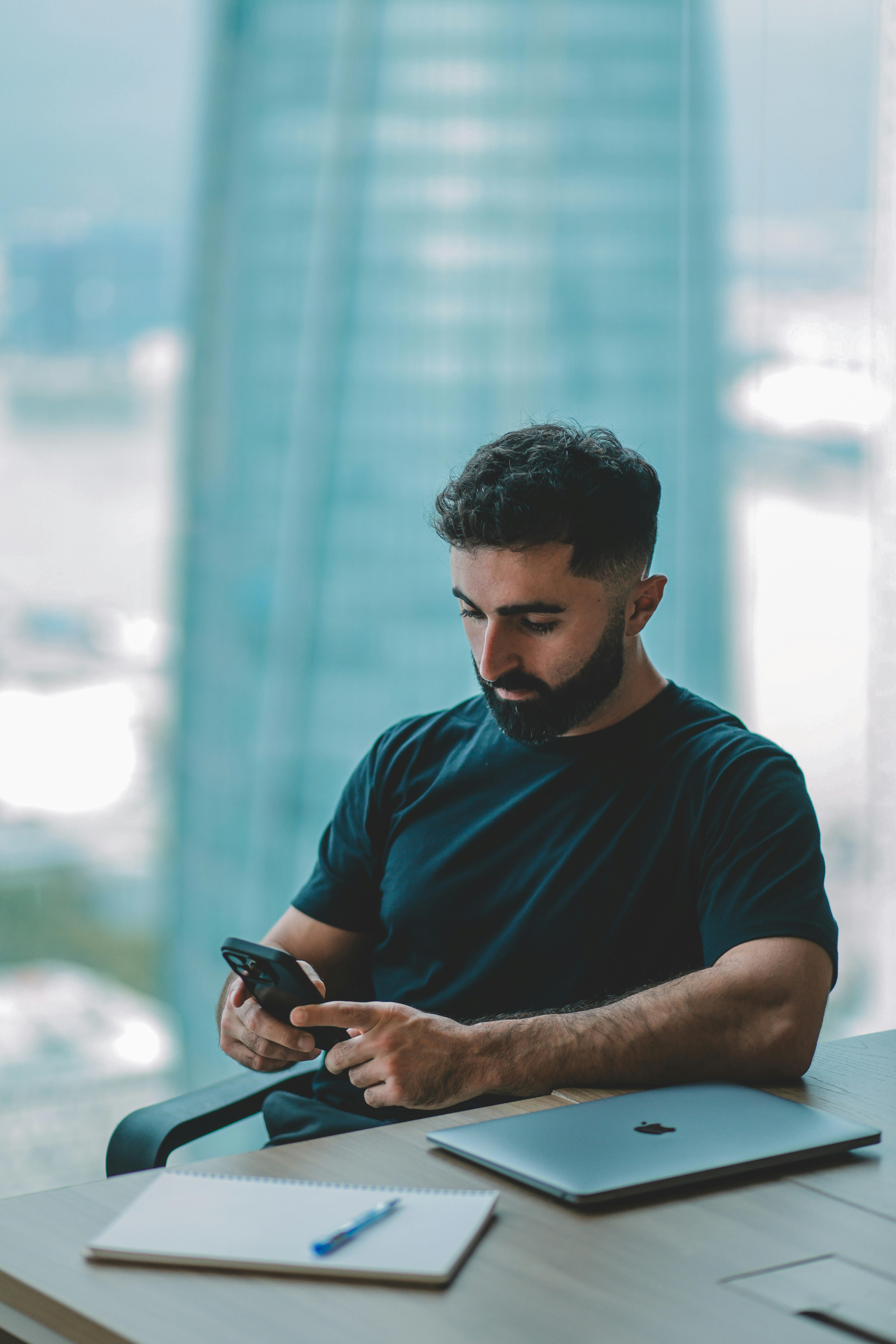Man looking at his phone with laptop on desk.