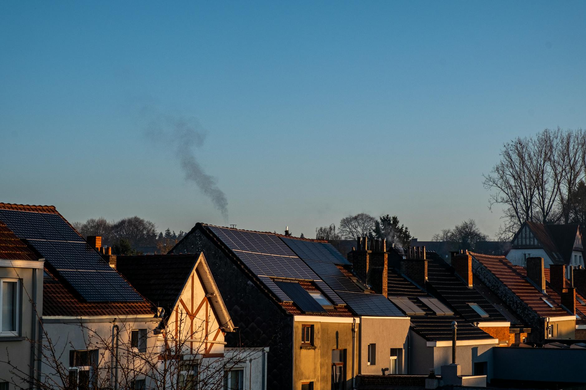 Suburban houses at golden hour with solar panels on rooftops and smoke rising from a chimney