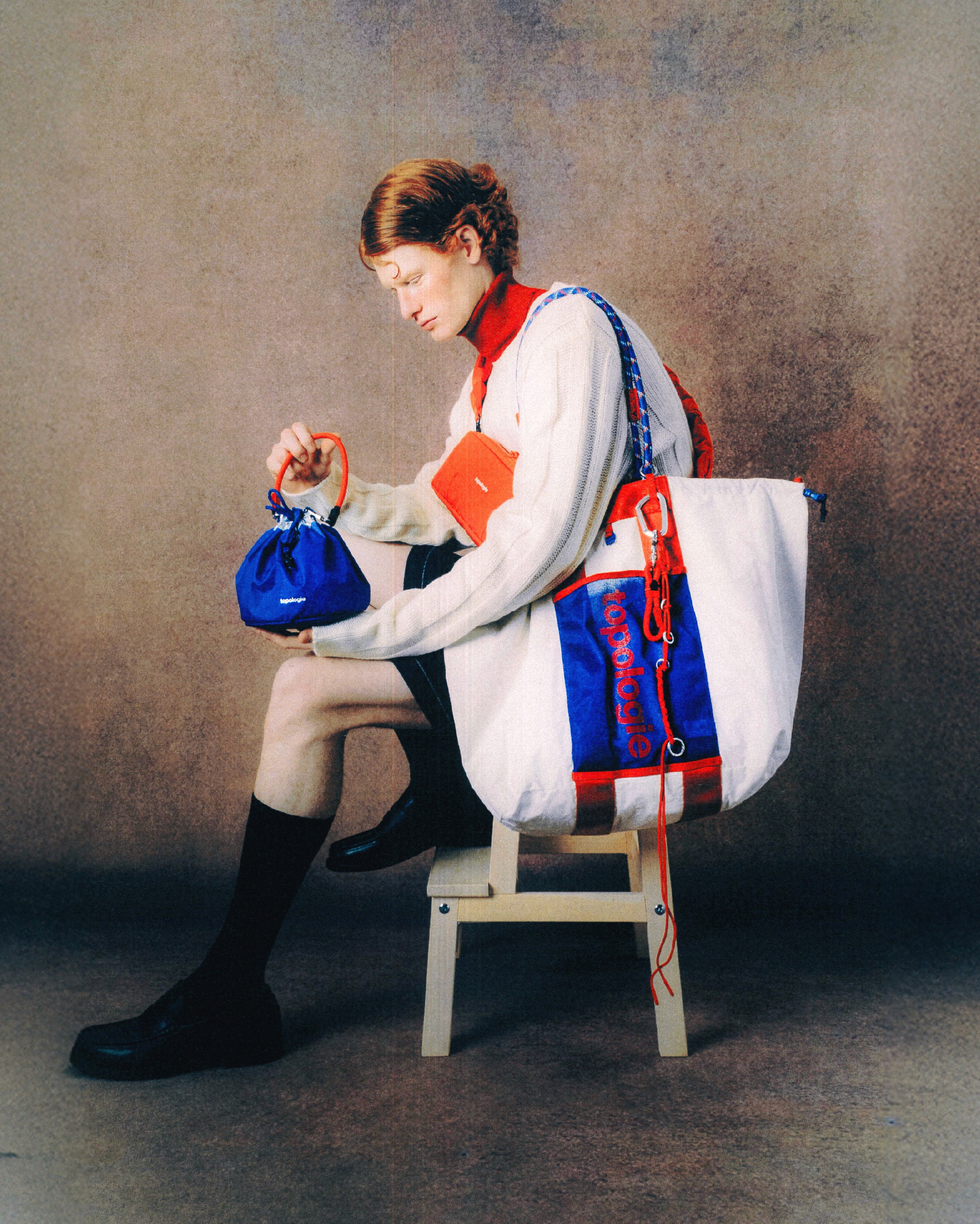 Un mannequin assis et vu de côté porte différents types de sacs siglés Topologie