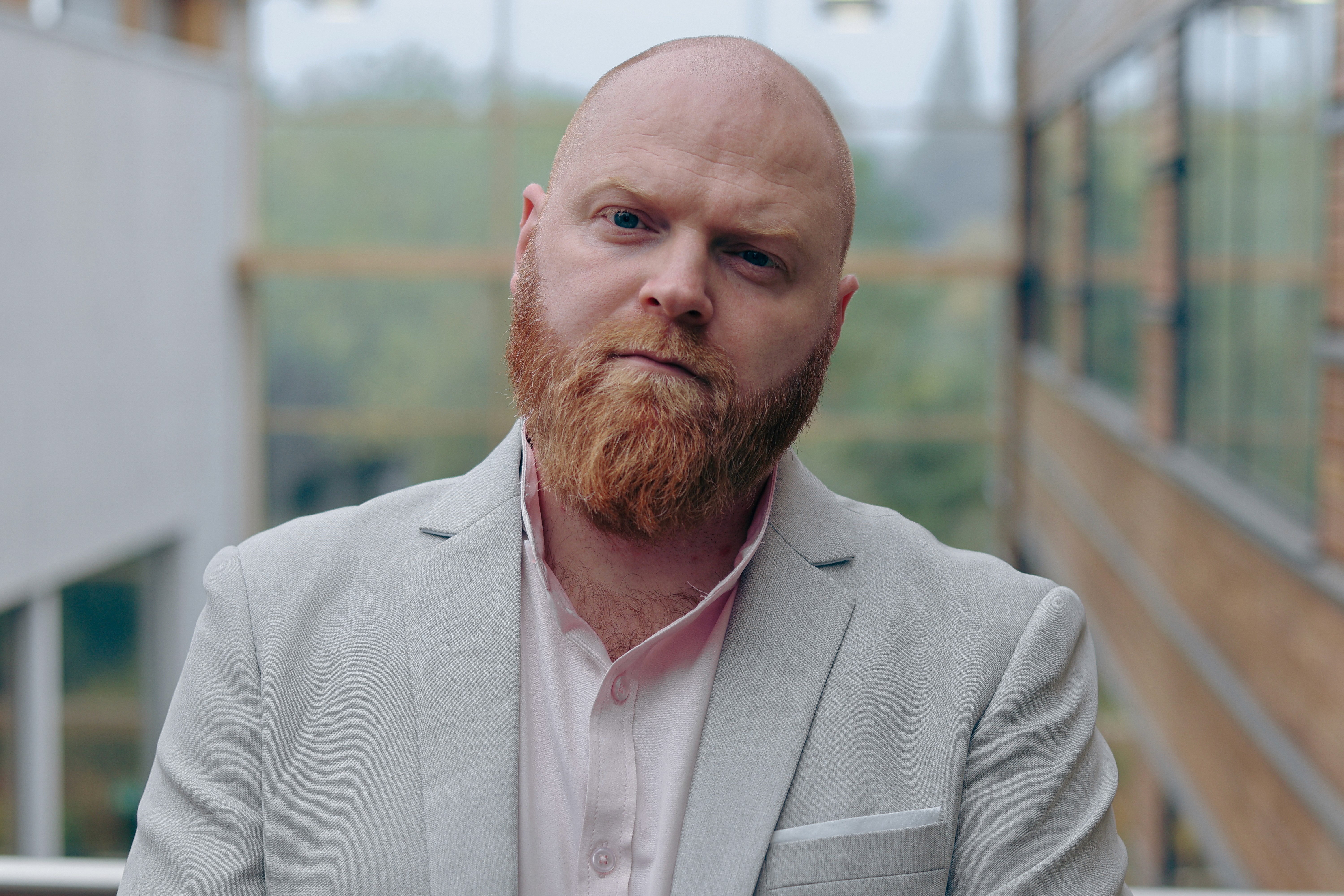A young person with curly hair smiles at the camera while sitting in front of a laptop against a dark background.