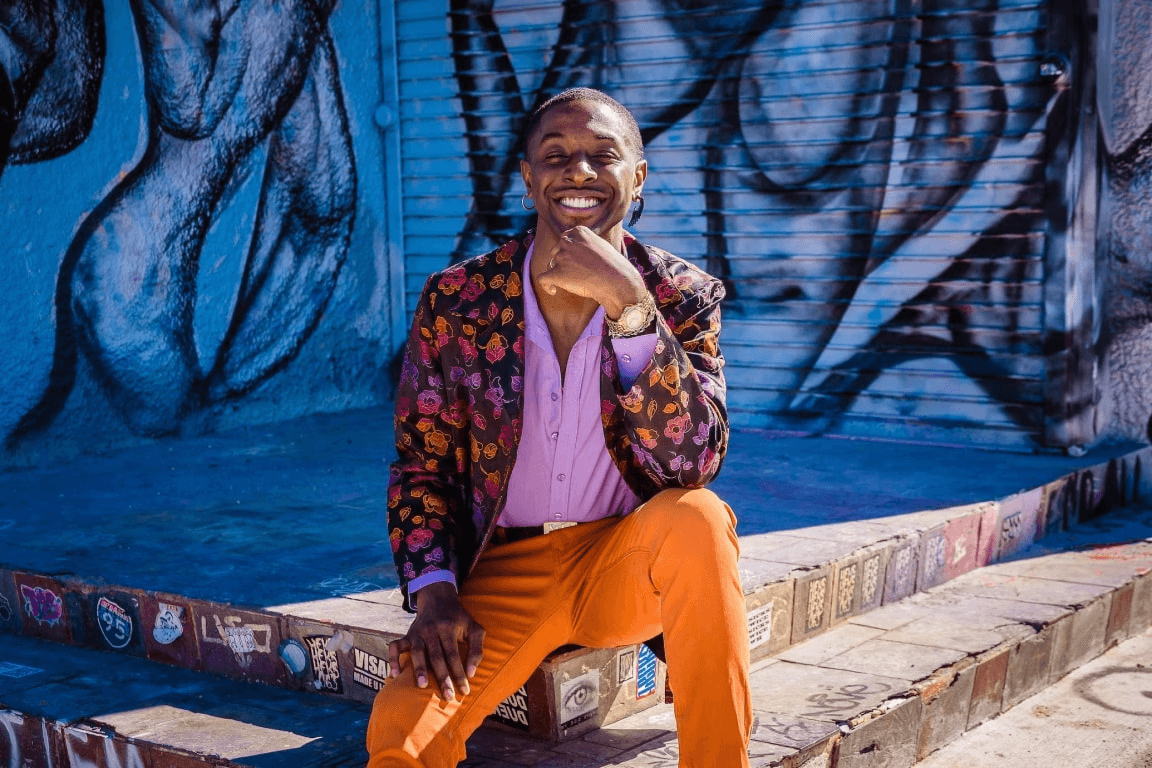 man smiling in a colorful outfit sitting on stairs with grafiti art behind him