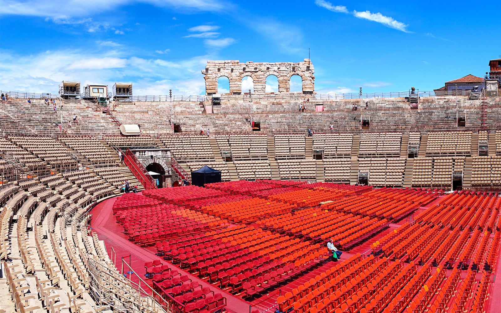 Verona Arena seating area with red chairs under a blue sky.