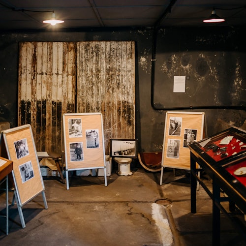 A dimly lit room with photo displays on easels, a framed picture on the floor, and glass-top display cases.