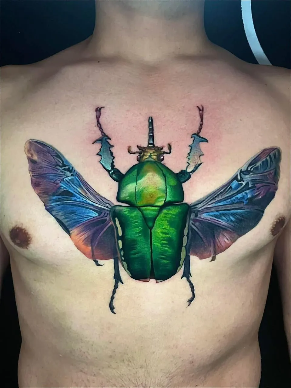 Color realism beetle tattoo on chest with blue wings at Calavera Ink Berlin