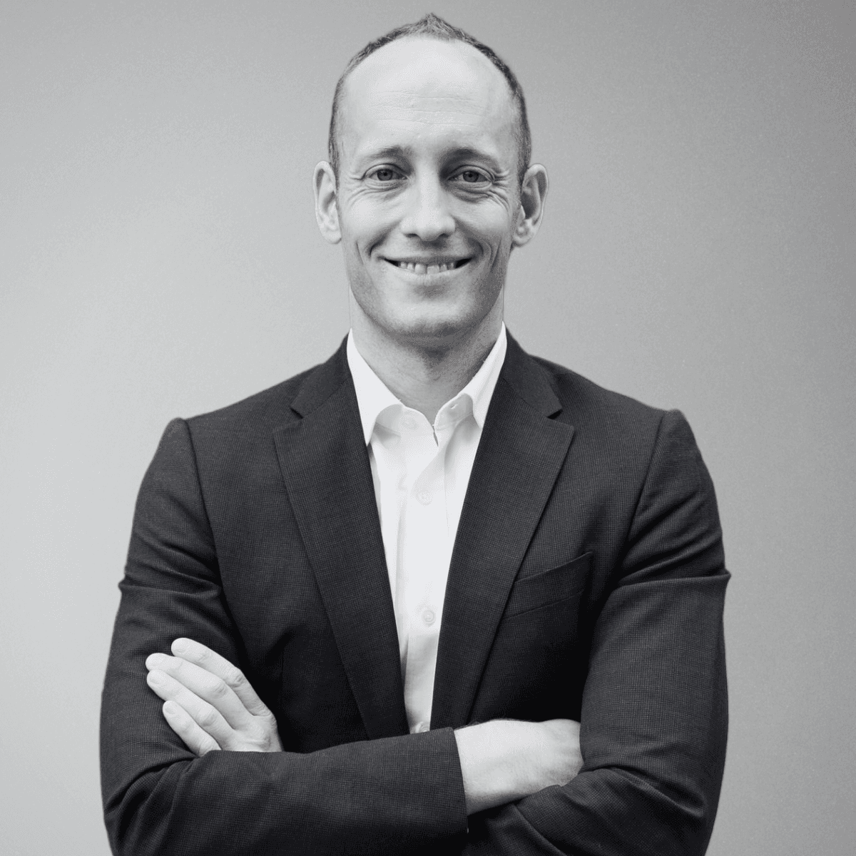 black and white photo of the upper part of a man in a suit and white shirt without tie and with his arms crossed. this is the CEO of BeyondTrucks, Hans Galland