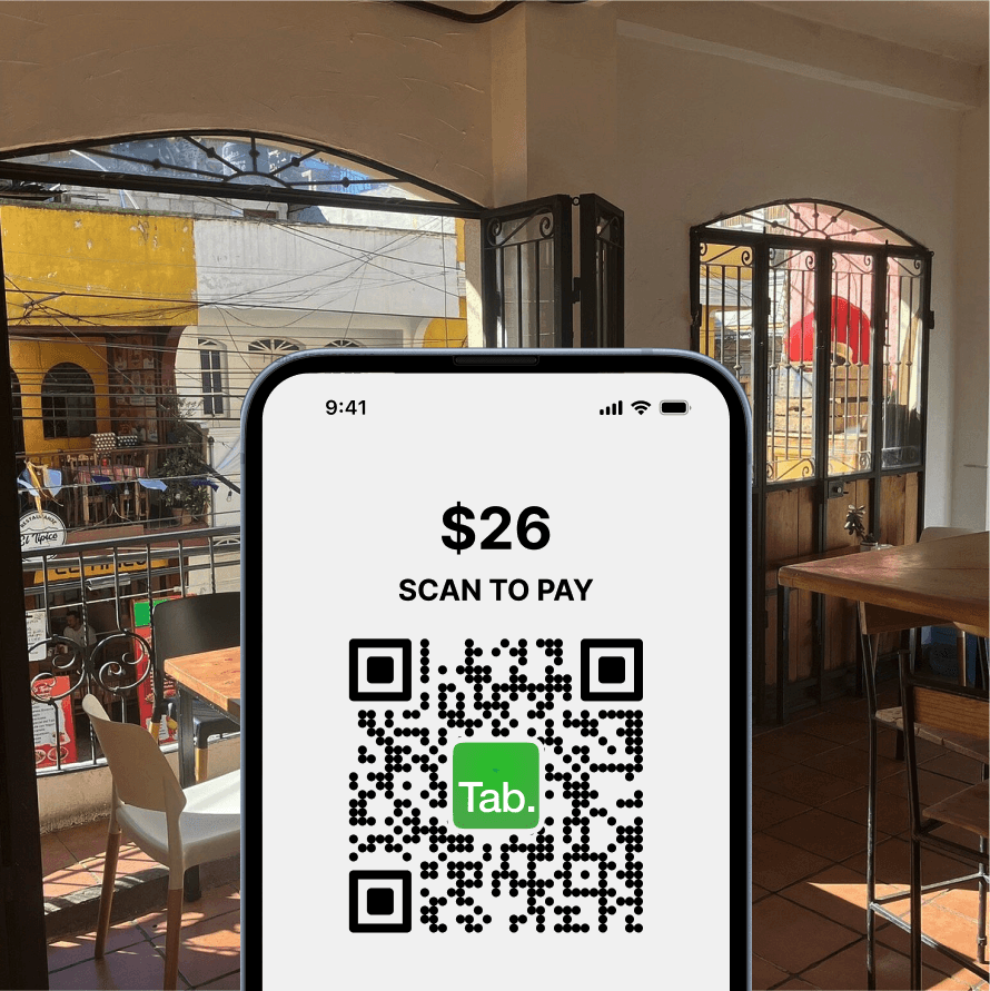 An image of a QR code. Above it says "Scan to Pay". There is a restaurant in the background.