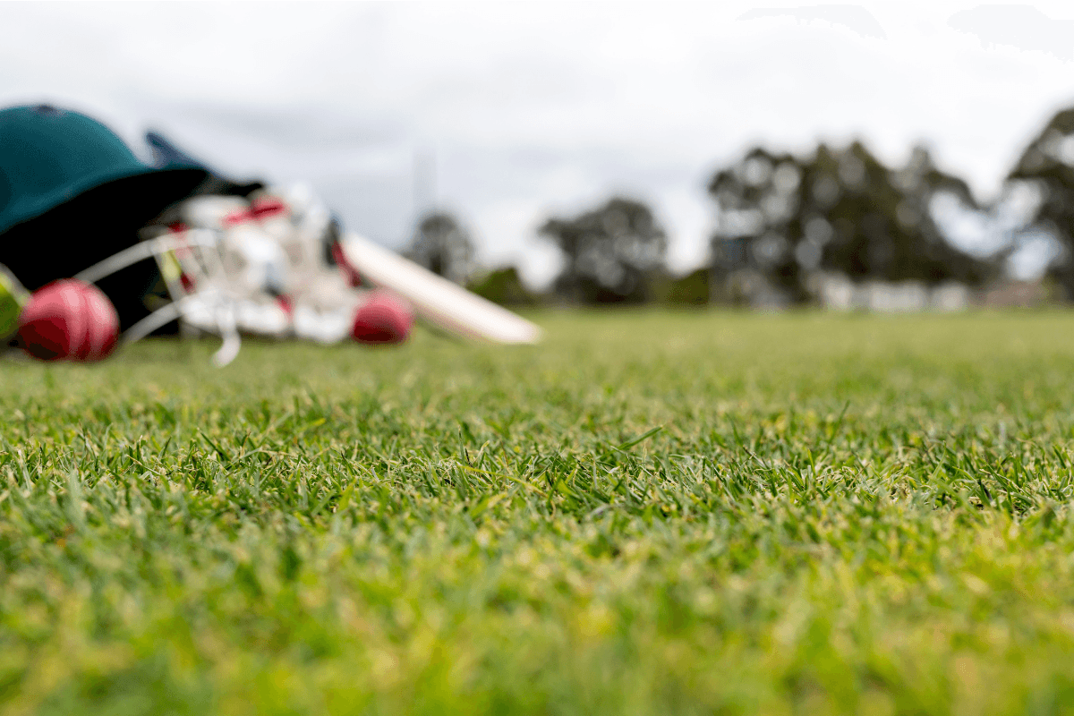 Cricket helmet, pads and match balls laid out on the boundary grass before a club match