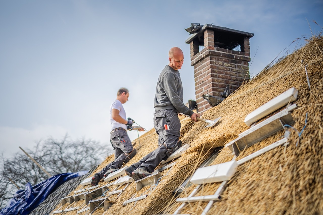 Rietdekkers van Rietdekkersbedrijf Van Dijk werken zorgvuldig aan de afwerking van een rieten dak