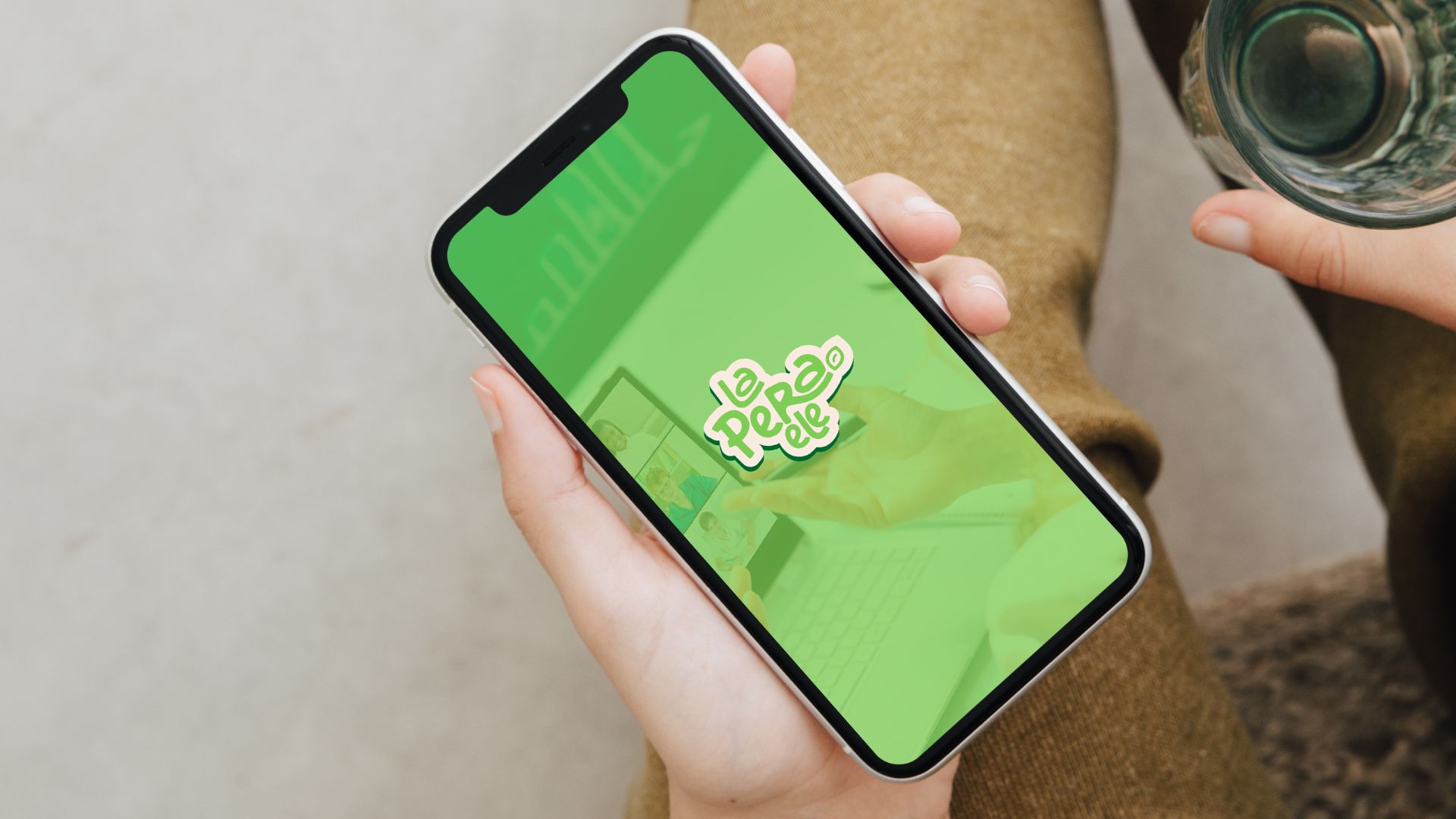 Brand identity for La Pera ELE displayed in a phone held by someone with brown pants having a glass of water on the other hand