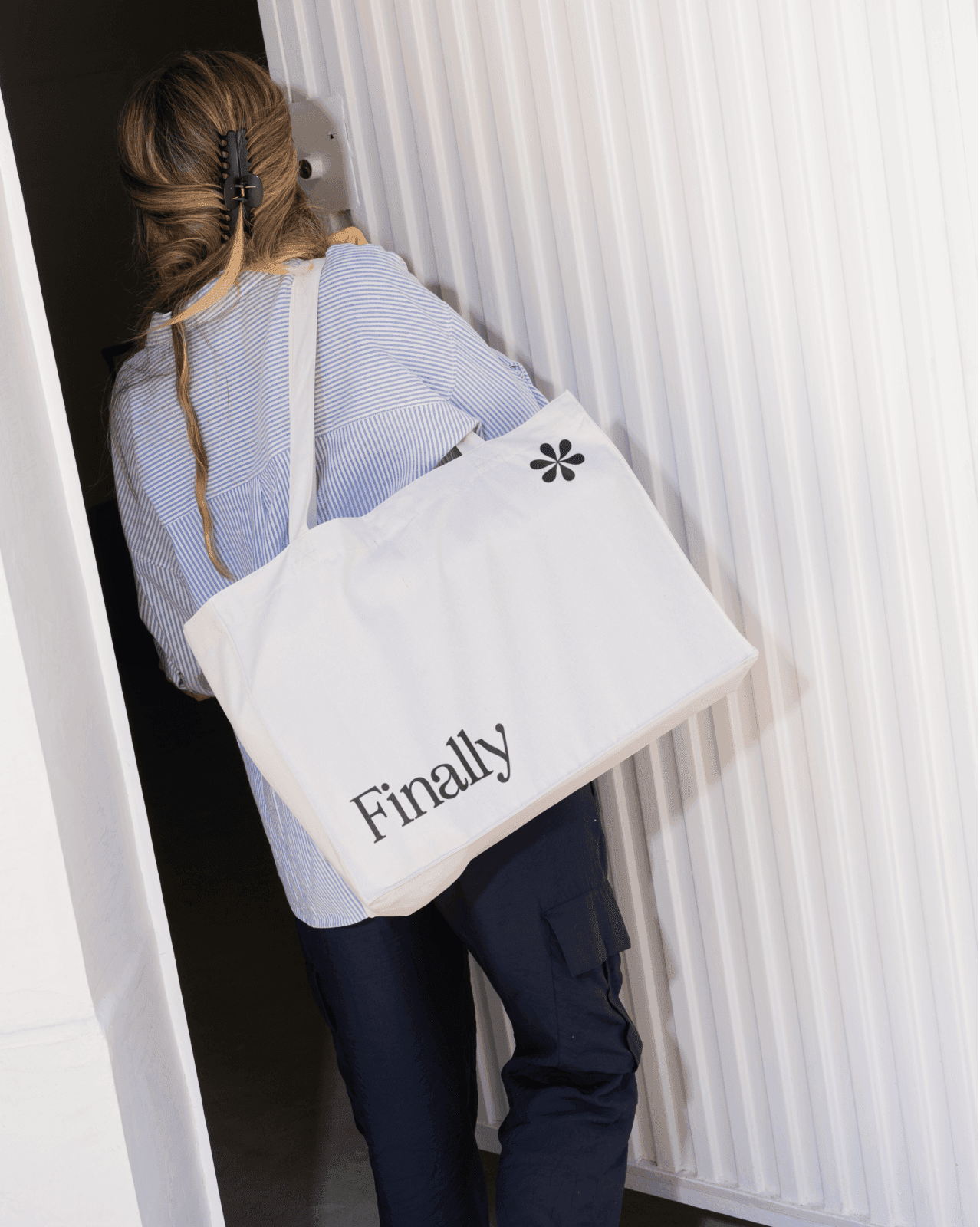 Person carrying a white tote bag with the word "Finally" printed on it.