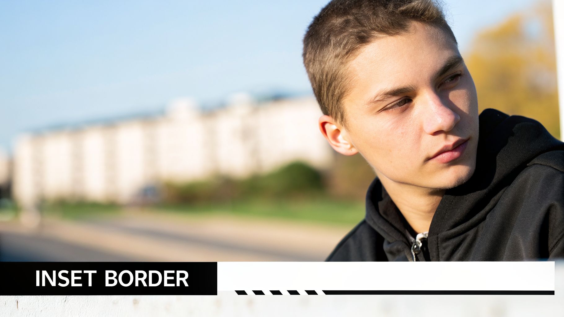 A young man in a black hoodie looks thoughtfully to the side against a blurred outdoor background.