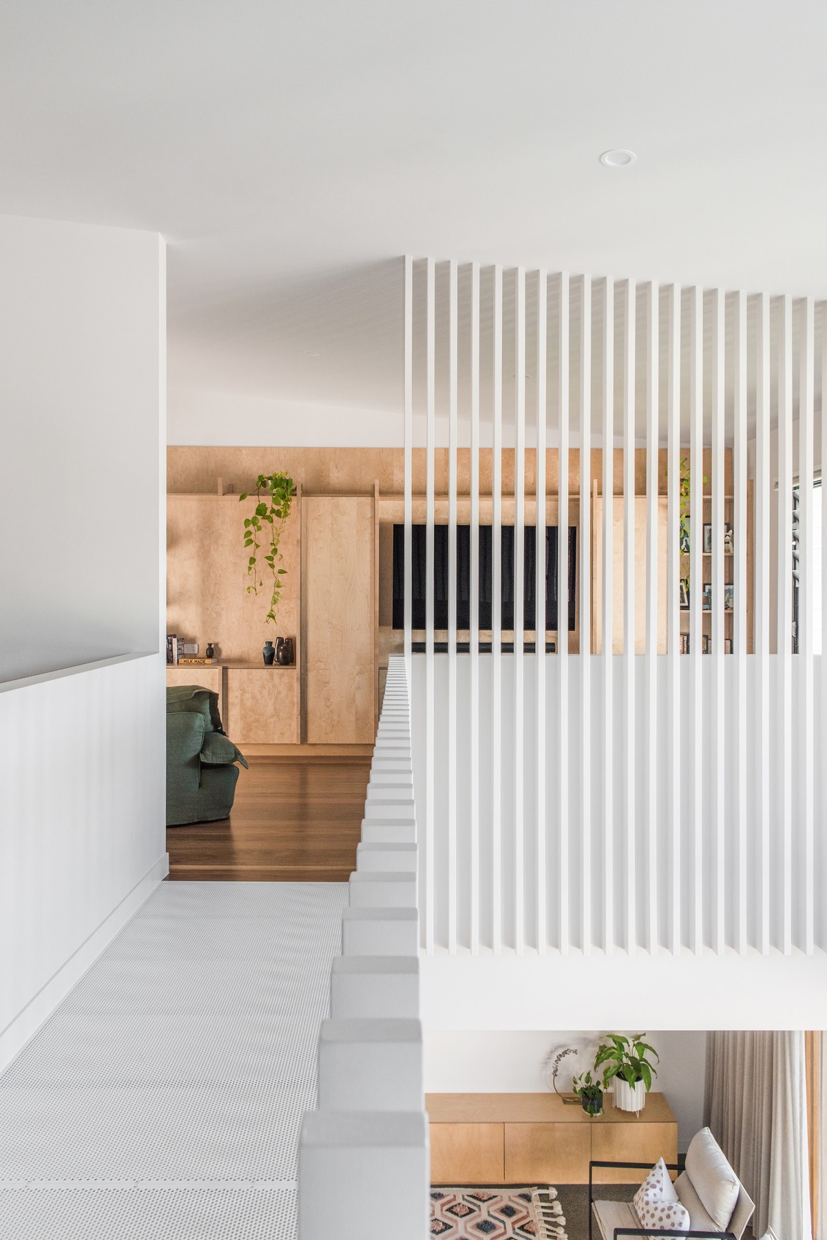 Upper-level walkway in Ridge House with white batten screening overlooking the double-height living space and timber-lined interior beyond.