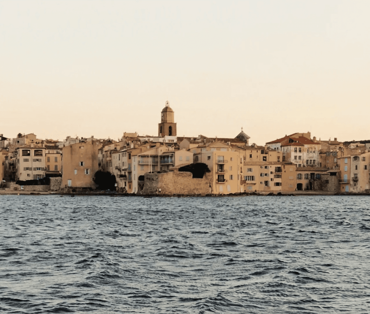 Coastal view of Saint-Tropez bathed in golden evening light, with the sea in the foreground.