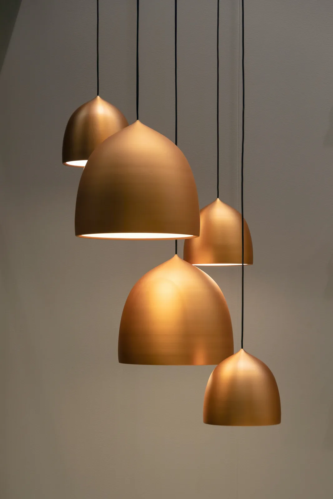 Cluster of five brushed copper pendant lamps hanging from ceiling