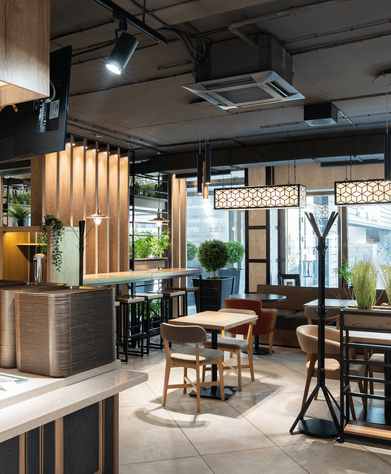 Salle de restaurant lumineuse et accueillante avec des tables en bois, des fauteuils confortables et une décoration végétale moderne.