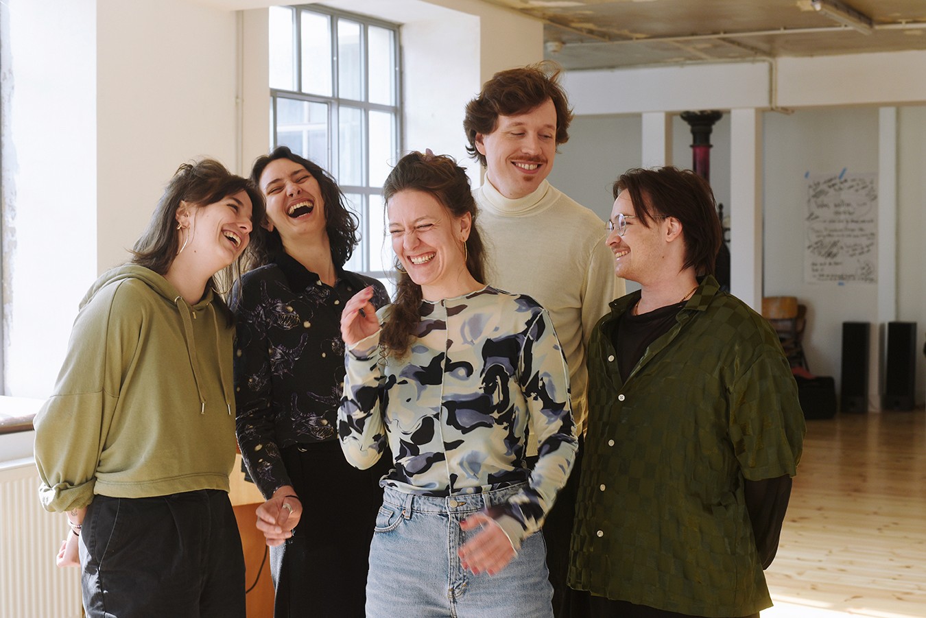 A group of five young adults poses together in a bright, modern indoor space, smiling and enjoying their time.