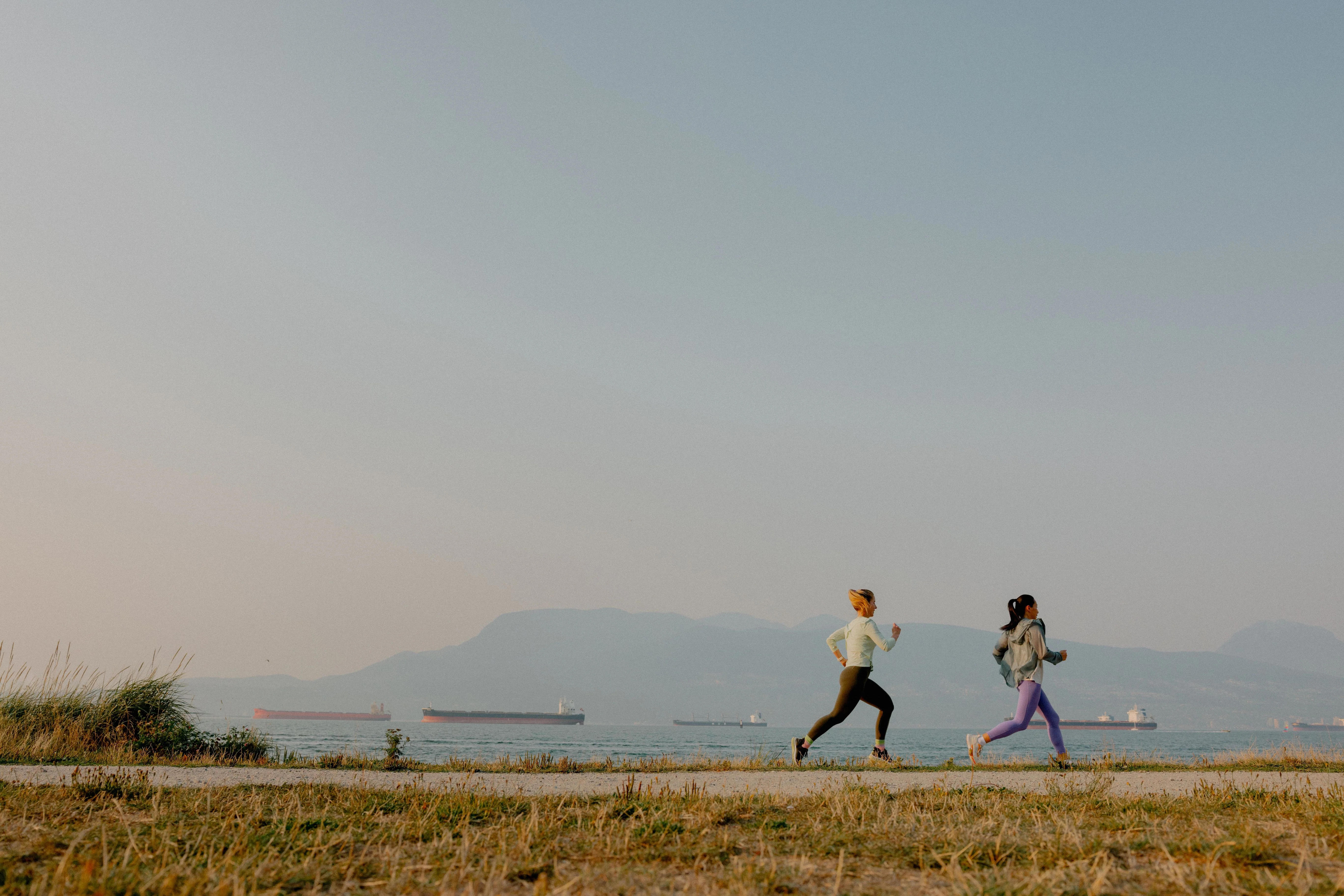 Two women running on waterfront trail in Vancouver, Canada. Mountains and boats in the background
