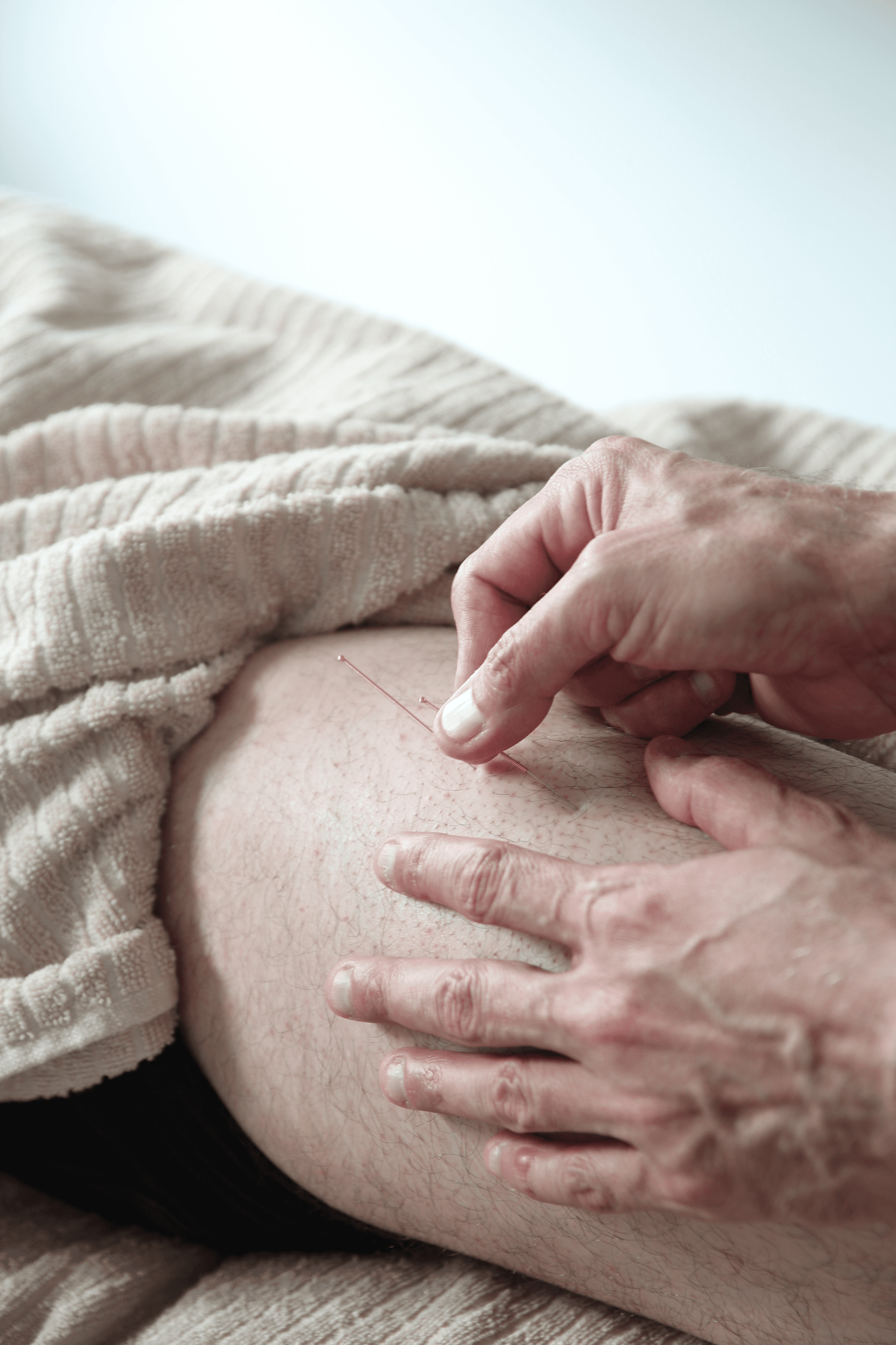 Woman in a towel applying pink under-eye gel patches while looking into a mirror on a vanity table