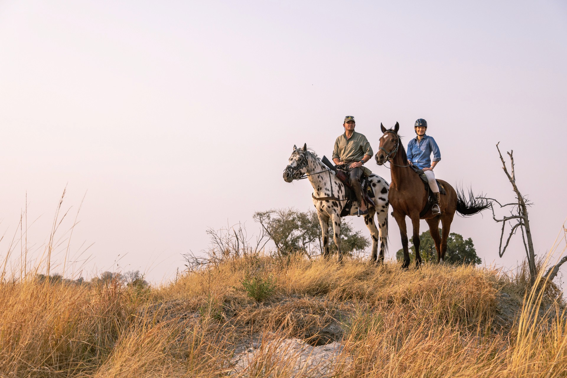 Kujwana Delta Ride, Okavango Delta, Botswana. Två ryttare till häst på ridsafari står på en höjd och blickar ut över landskapet.