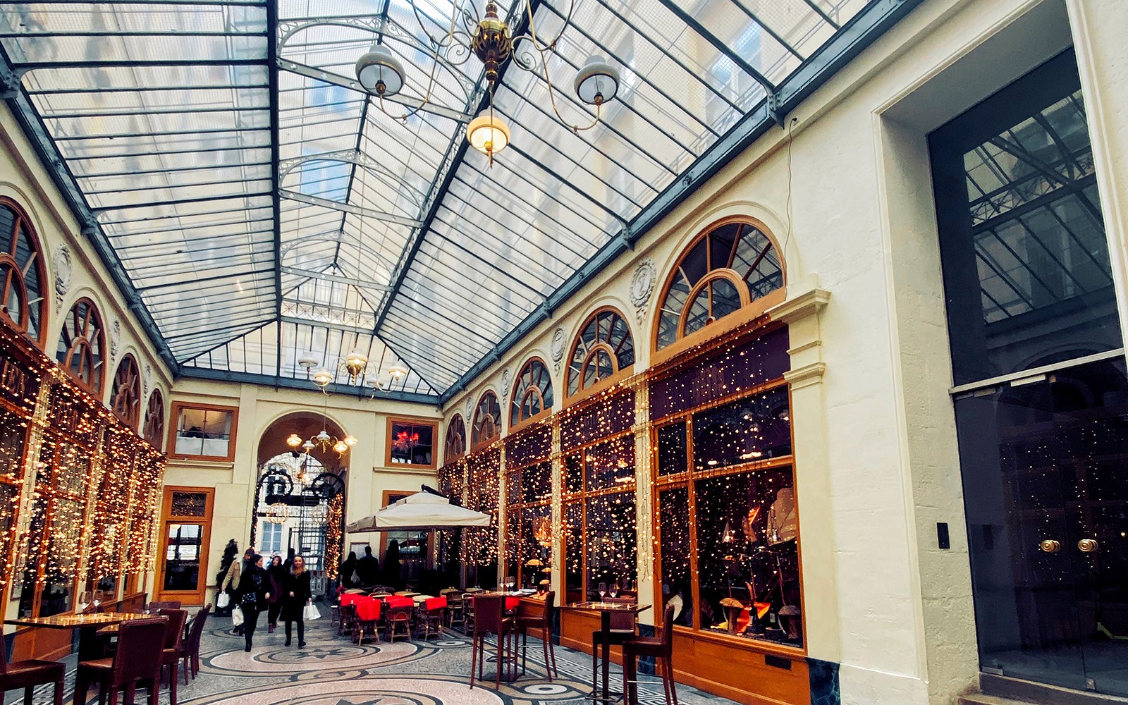 Passage couvert à Paris avec toit en verre, fenêtres cintrées, et des passants.