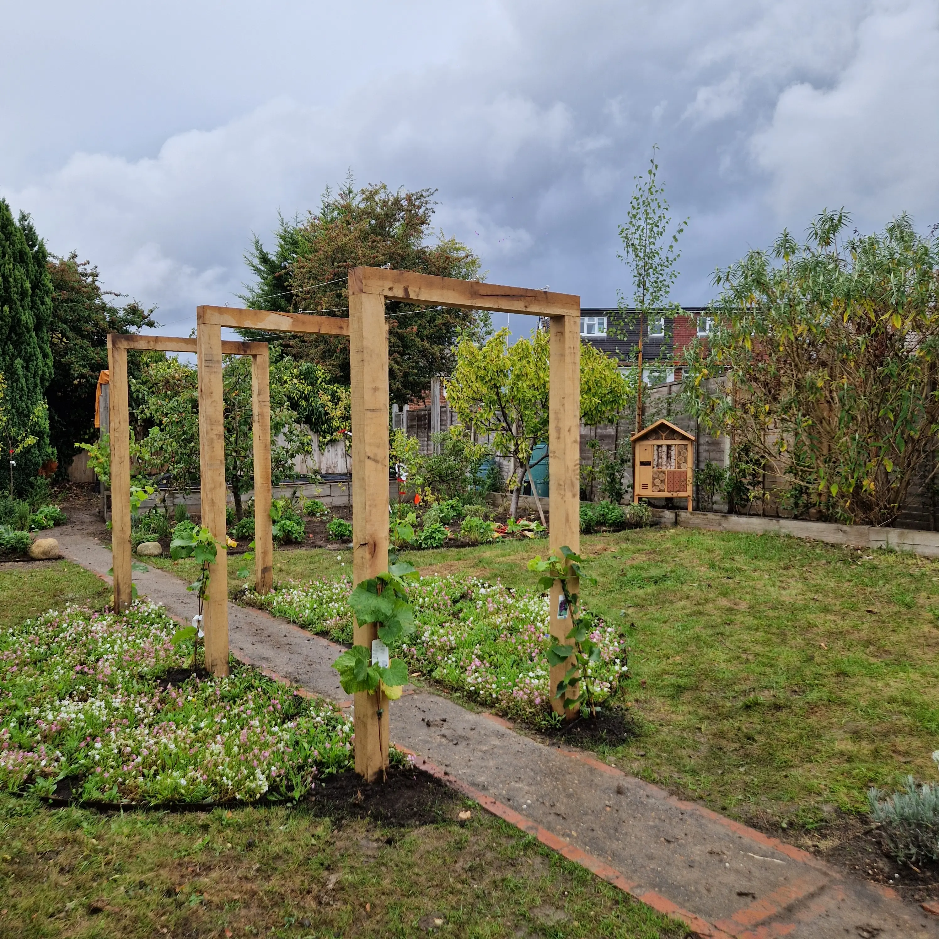 A garden with a wooden trellis, path, and green plants under a partly cloudy sky.