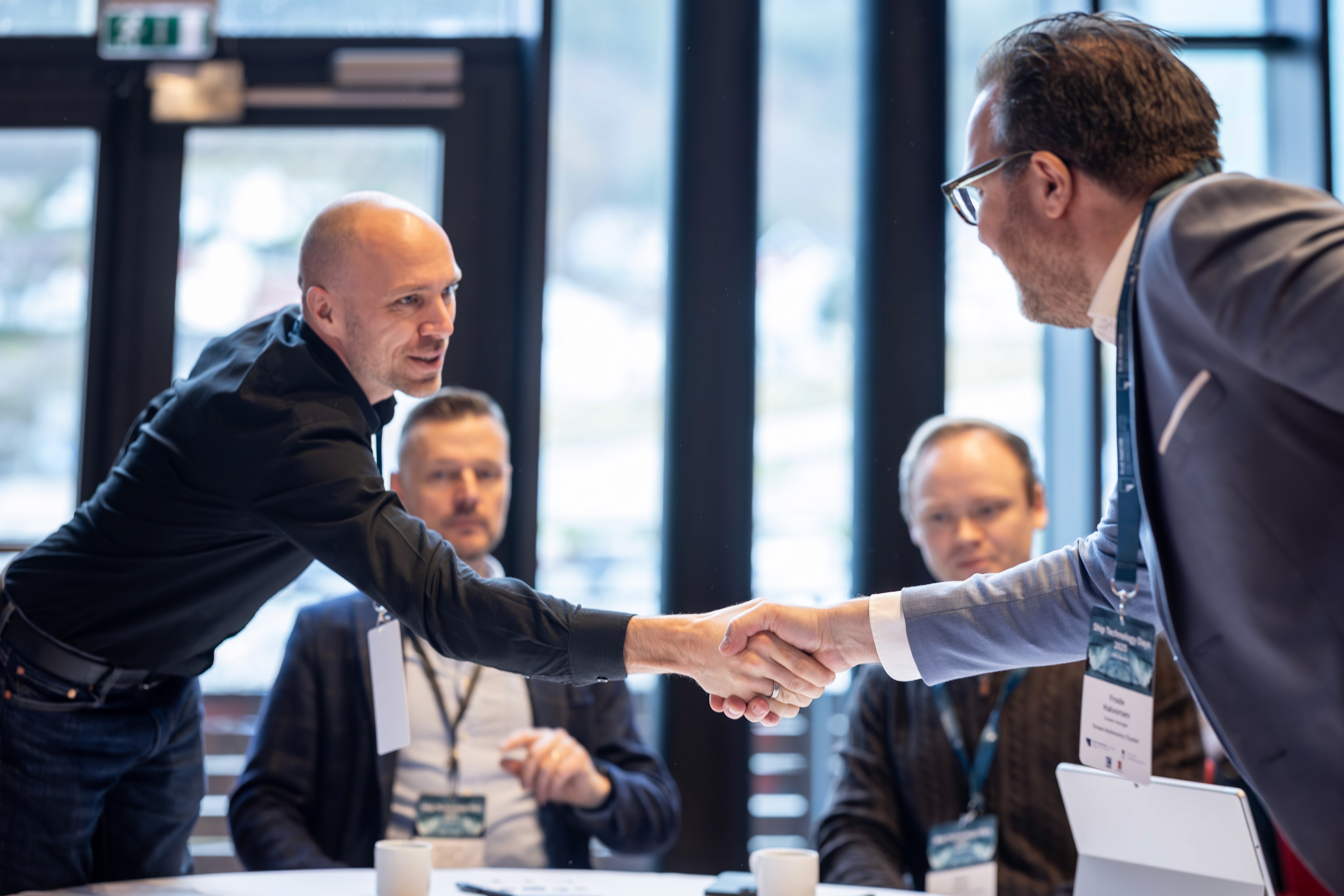 Four business professionals engaging in a handshake during a meeting at a modern office setting.