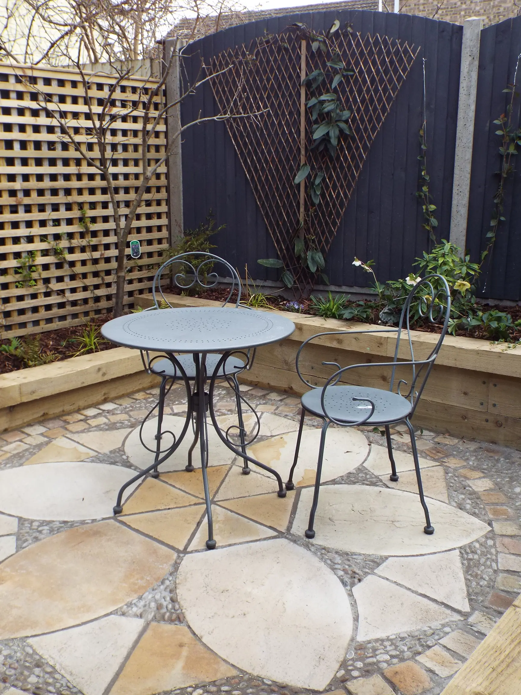 A small outdoor patio area featuring a round table and a chair against a natural stone background.