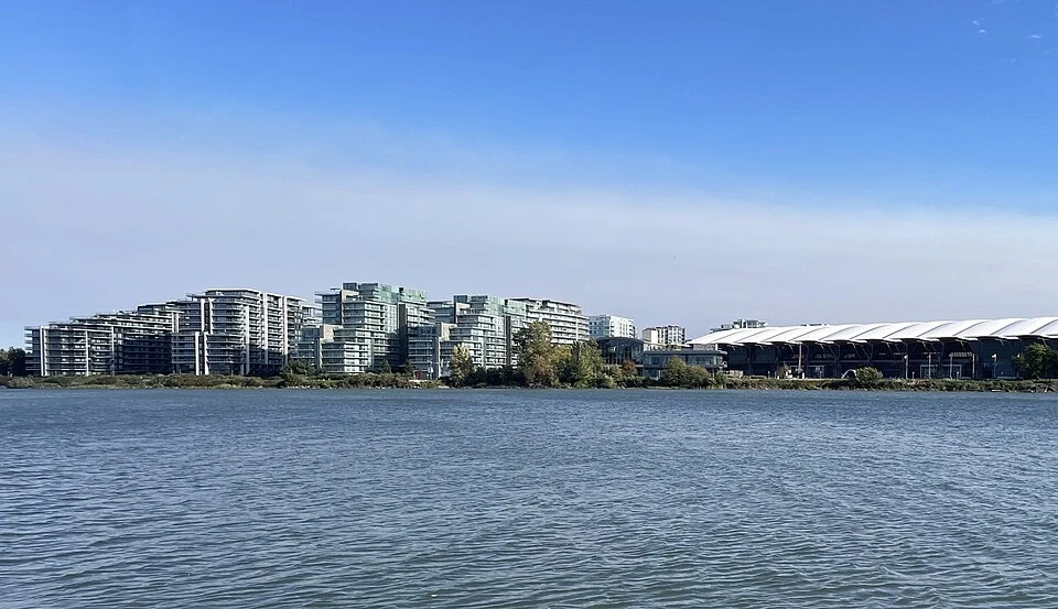 Waterfront view of Richmond, British Columbia, featuring modern high-rise residential buildings and the Richmond Olympic Oval along the shoreline.