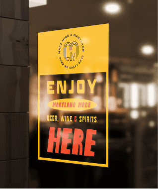 Yellow sign on a glass door reads: Enjoy Maryland made beer, wine & spirits here, with Baltimore branding above and a blurred indoor background.