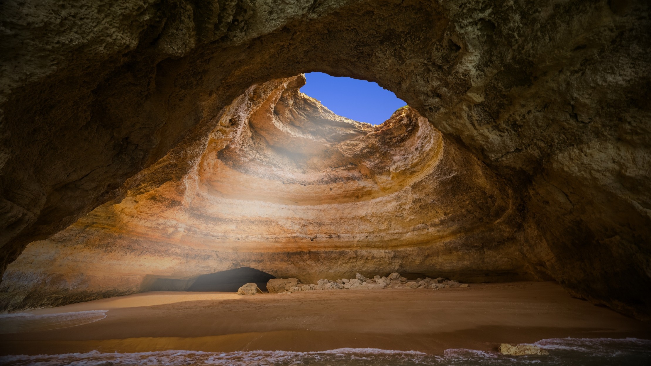 the sun is setting on the beach near the rocks