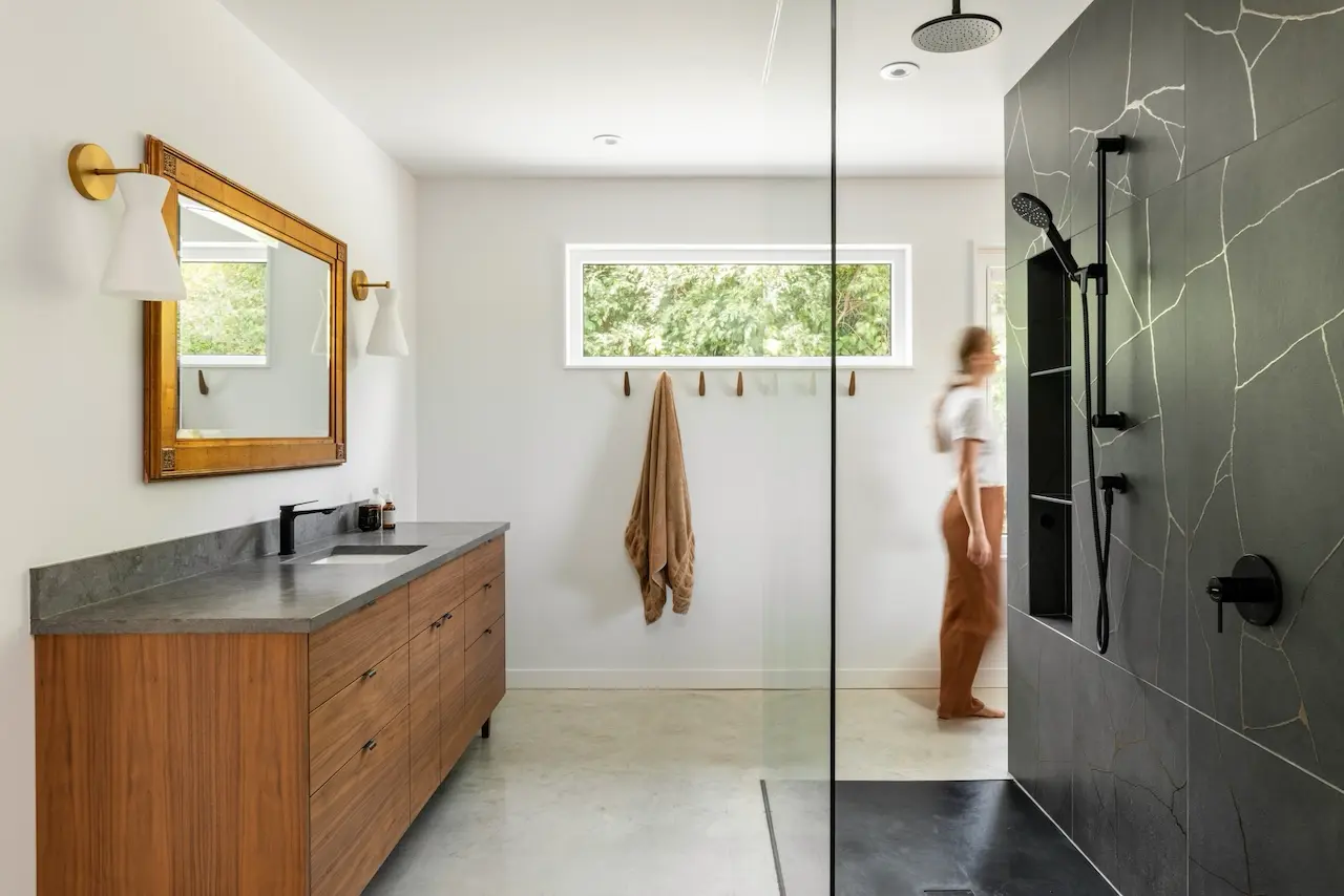 Modern two-story home with large glass windows, warmly lit interiors, and a balcony. Surrounded by trees and a manicured lawn at dusk. Cozy ambiance.