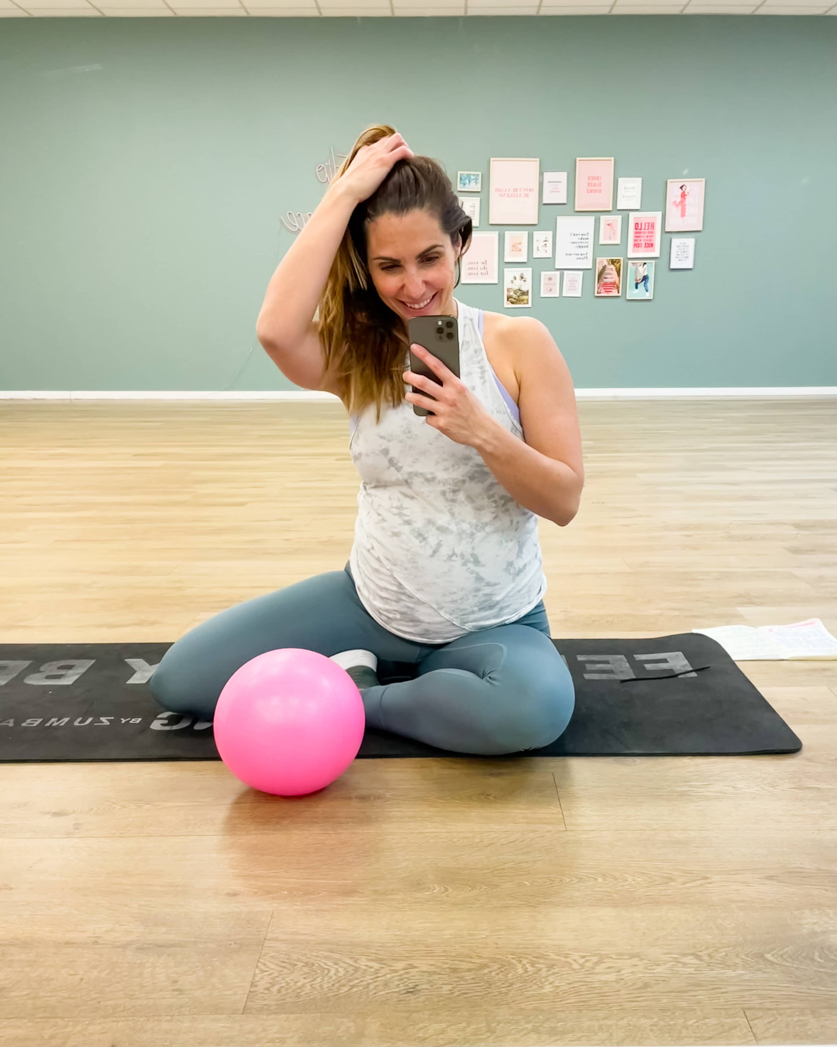 Matériel de sport grossesse : Caroline assise sur un tapis de sol en studio avec un petit ballon de Pilates prénatal.