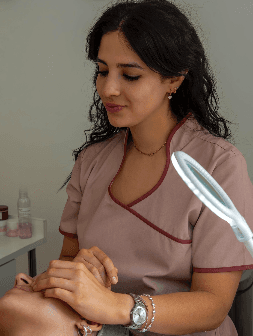 A woman lying on a massage bed, illuminated by soft sunlight streaming through a nearby window. A lush green plant in the background enhances the peaceful and rejuvenating ambiance.