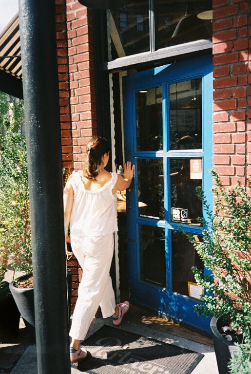 a woman in all white walking into a coffee shop with a blue door