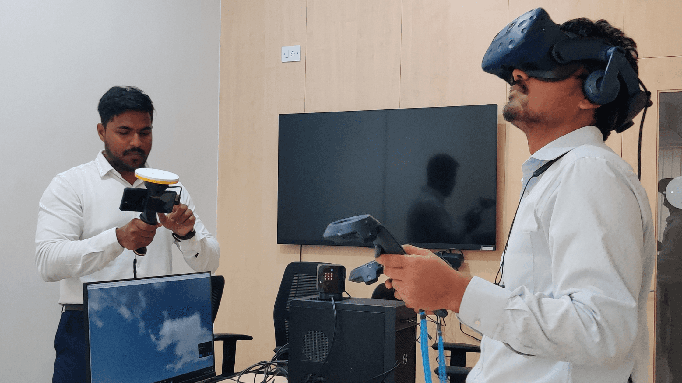 A man stands while two people sit at a table in an office setting, smiling and engaged in conversation. The mood is friendly and collaborative.