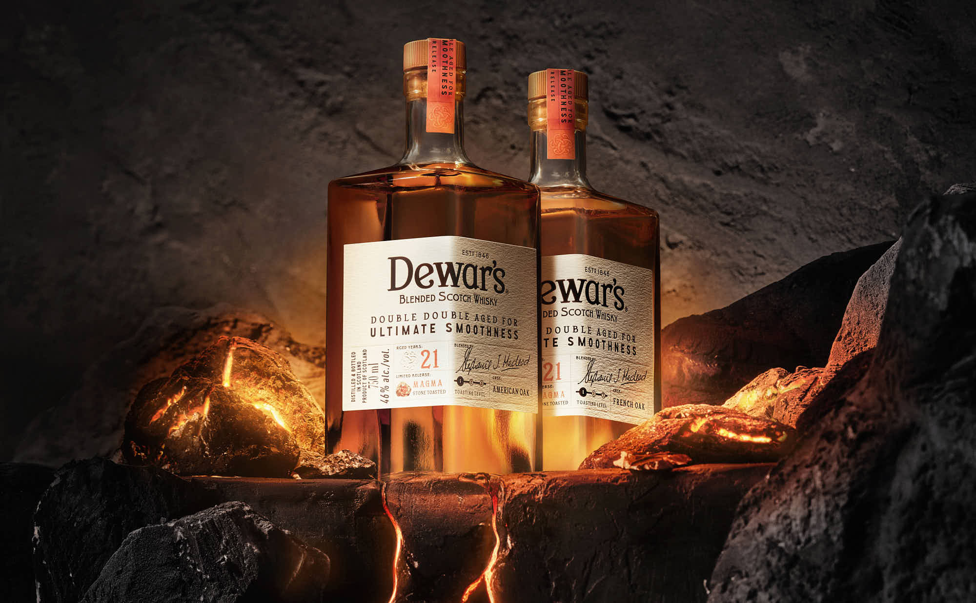 Two whiskey bottles stand on a rocky surface, surrounded by warm, flickering light against a dark background.