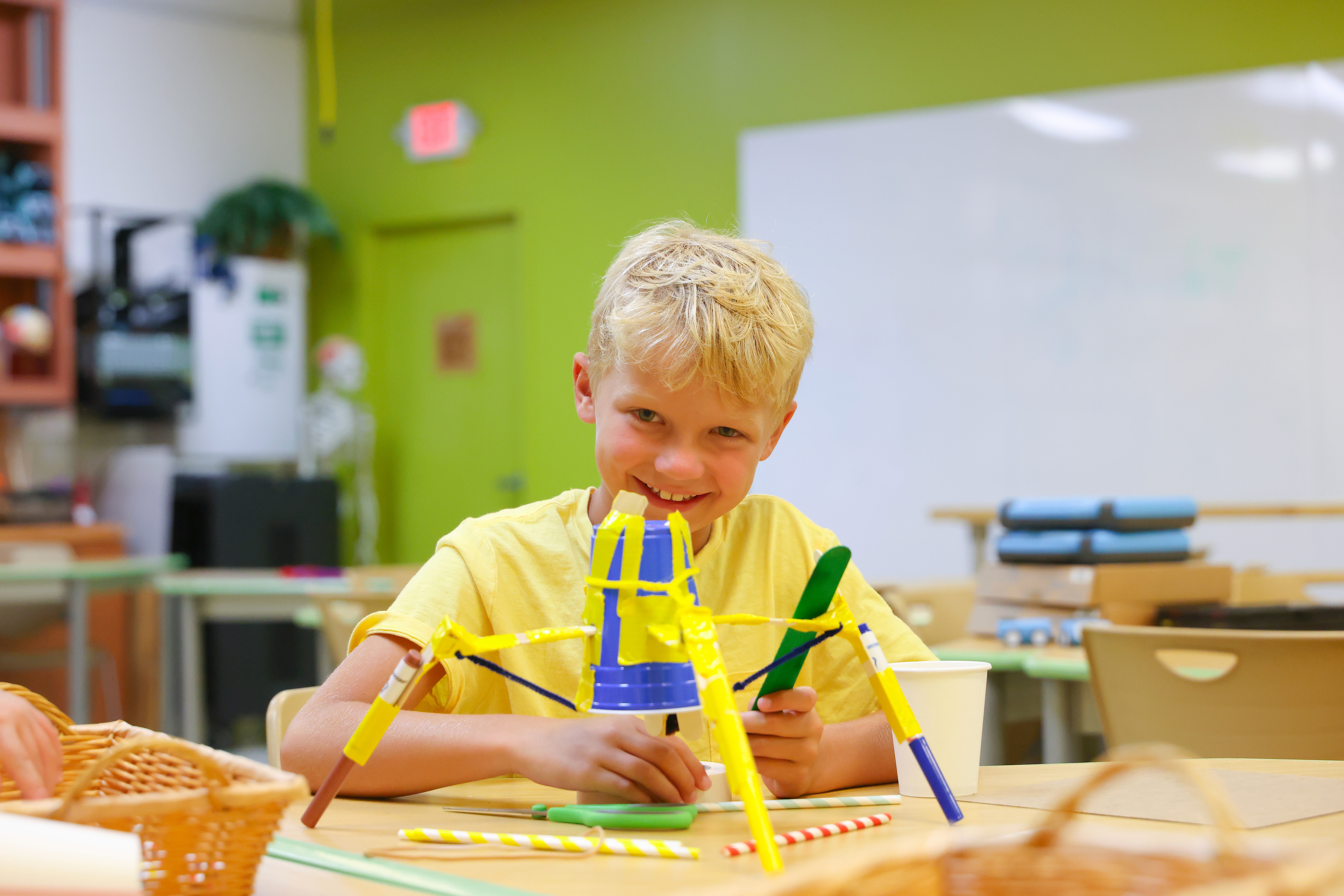 A boy creates a spider out of plastic cups, markers, tape and rubber bands.