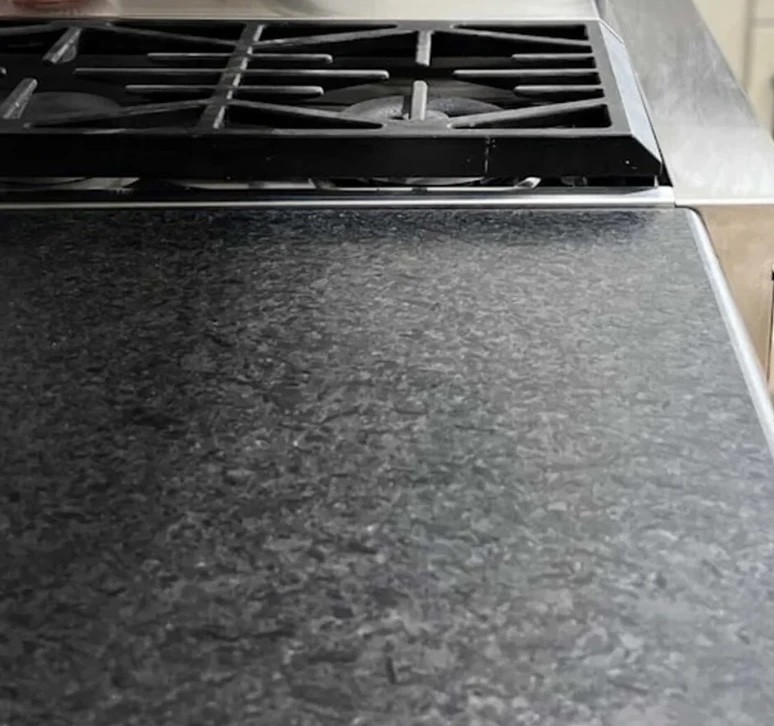 Black Pearl granite with a leathered finish: matte charcoal with a soft, textured surface and silver-gray flecks, next to a gas range